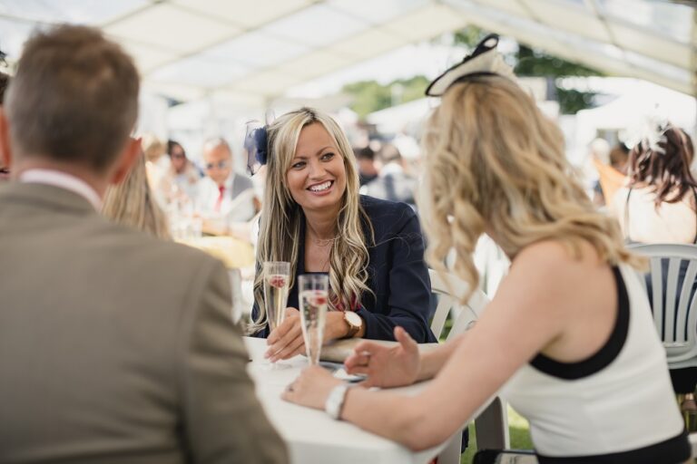 Couples enjoying a day at the races. Females enjoying a drink in an open marquee